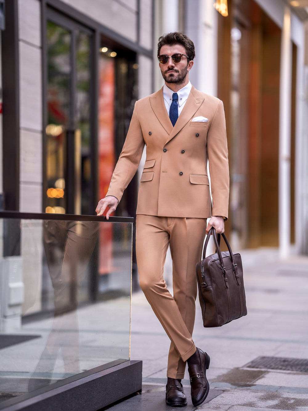 Man wearing a tan double-breasted suit for men by XAYWEAR with blue tie and brown leather shoes