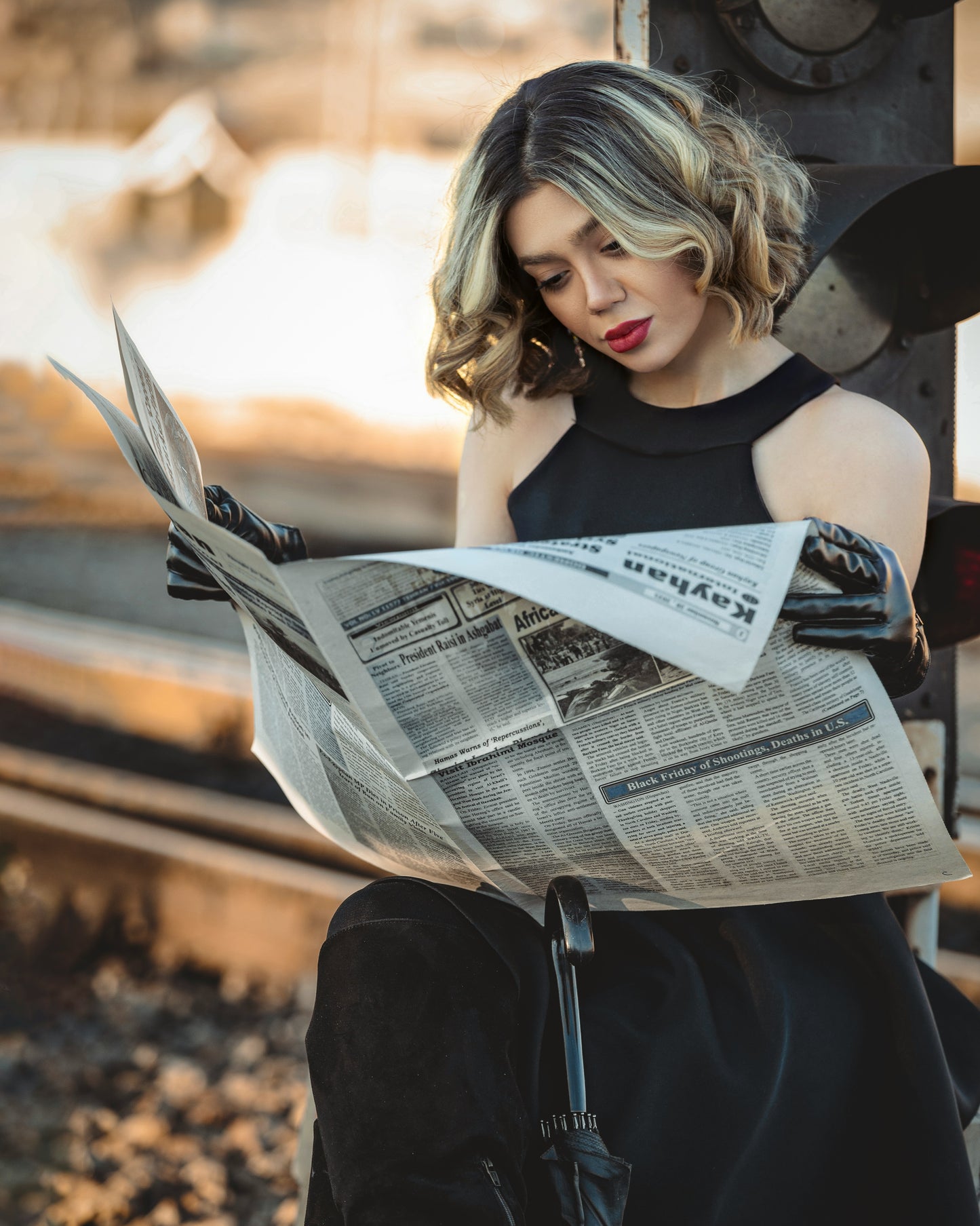 Woman wearing a black dress by XAYWEAR reading a newspaper while sitting outdoors