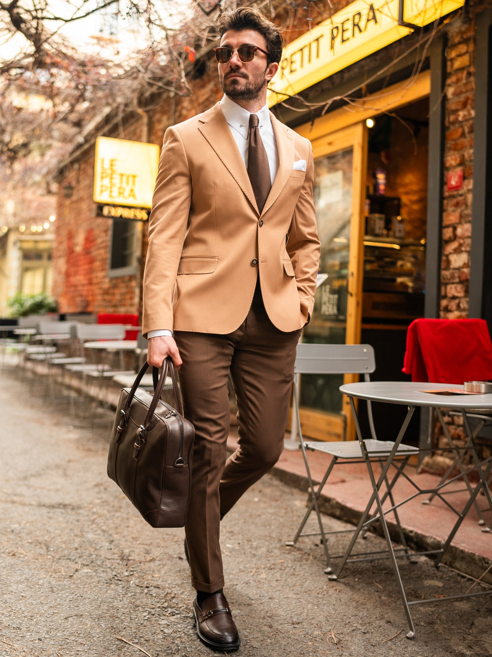 XAYWEAR stylish suit for men in tan blazer and brown pants carrying leather briefcase in urban setting