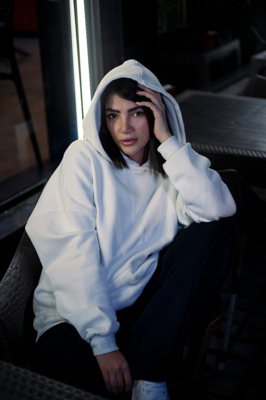 XAYWEAR white hoodie worn by woman sitting outdoors with hood up and relaxed pose