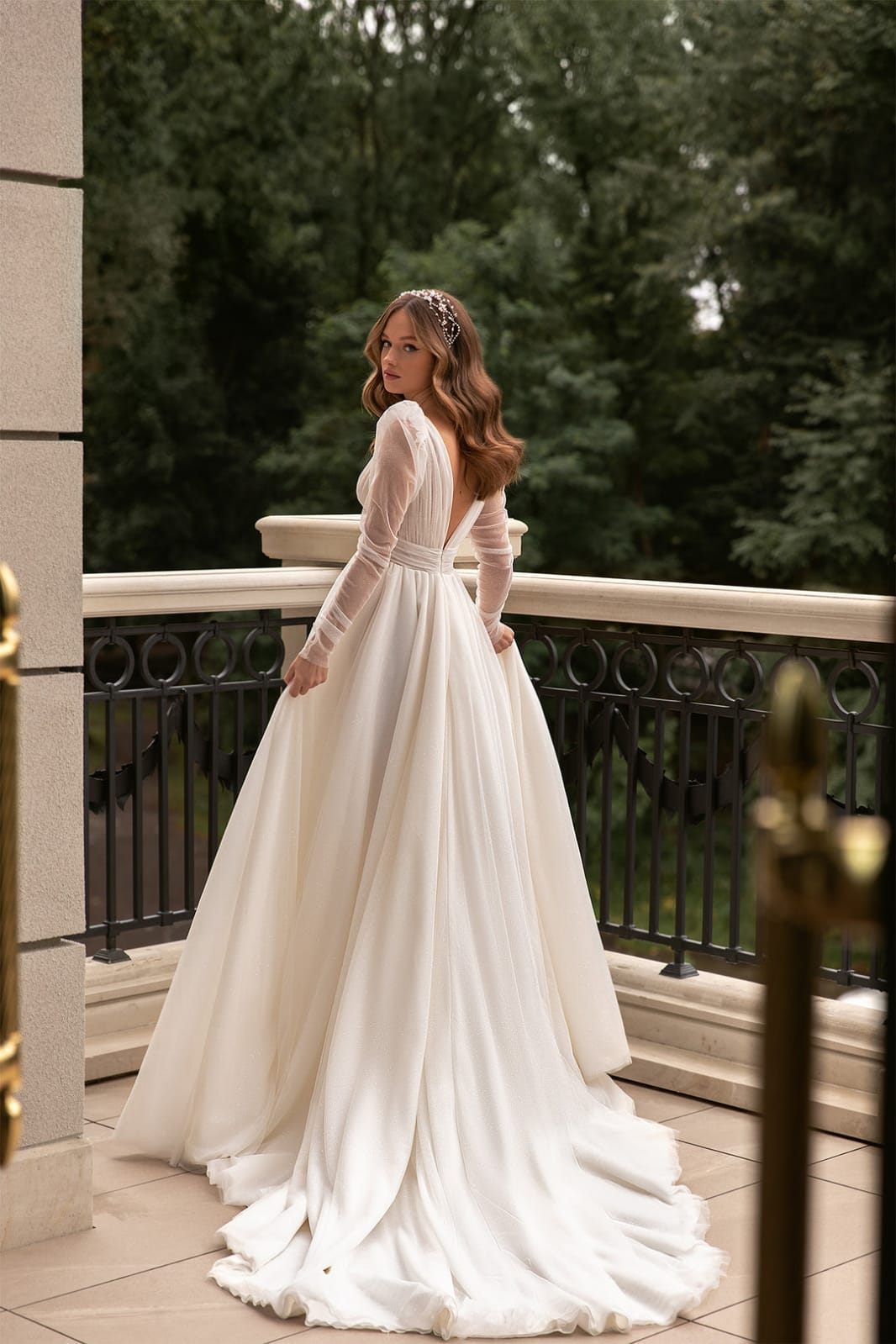 XAYWEAR bridal gown with long sheer sleeves and flowing train worn outdoors on balcony