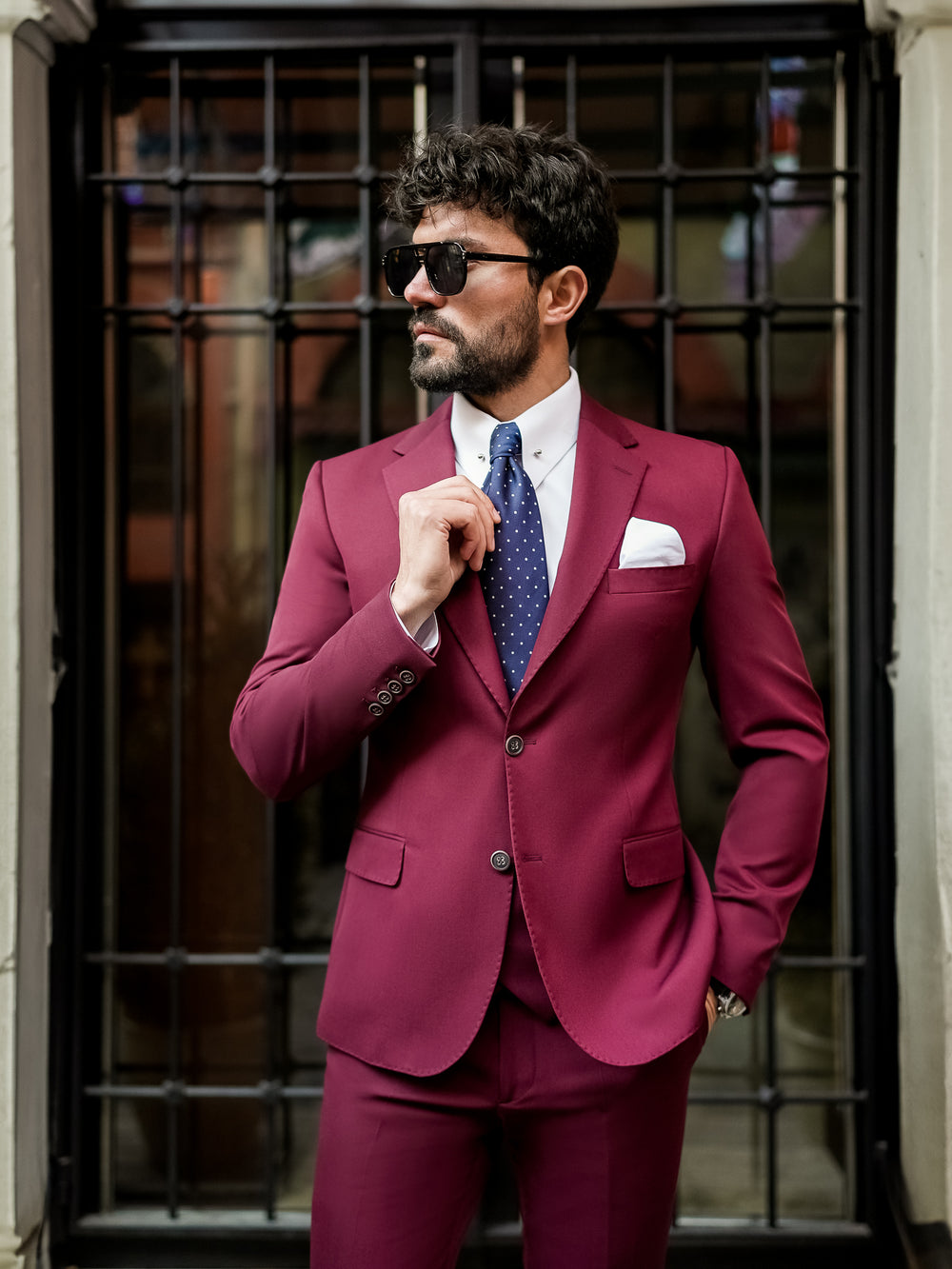 Man wearing a stylish burgundy suit for men with a white shirt and blue tie standing outdoors