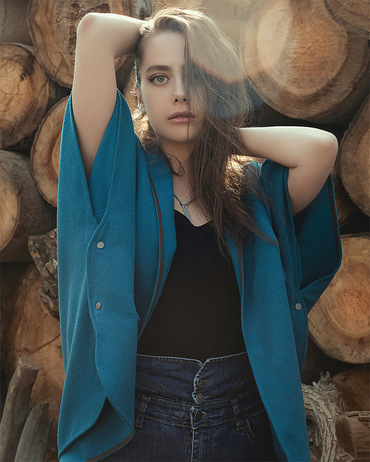 XAYWEAR teal cape jacket for women styled with black top and jeans against stacked logs background