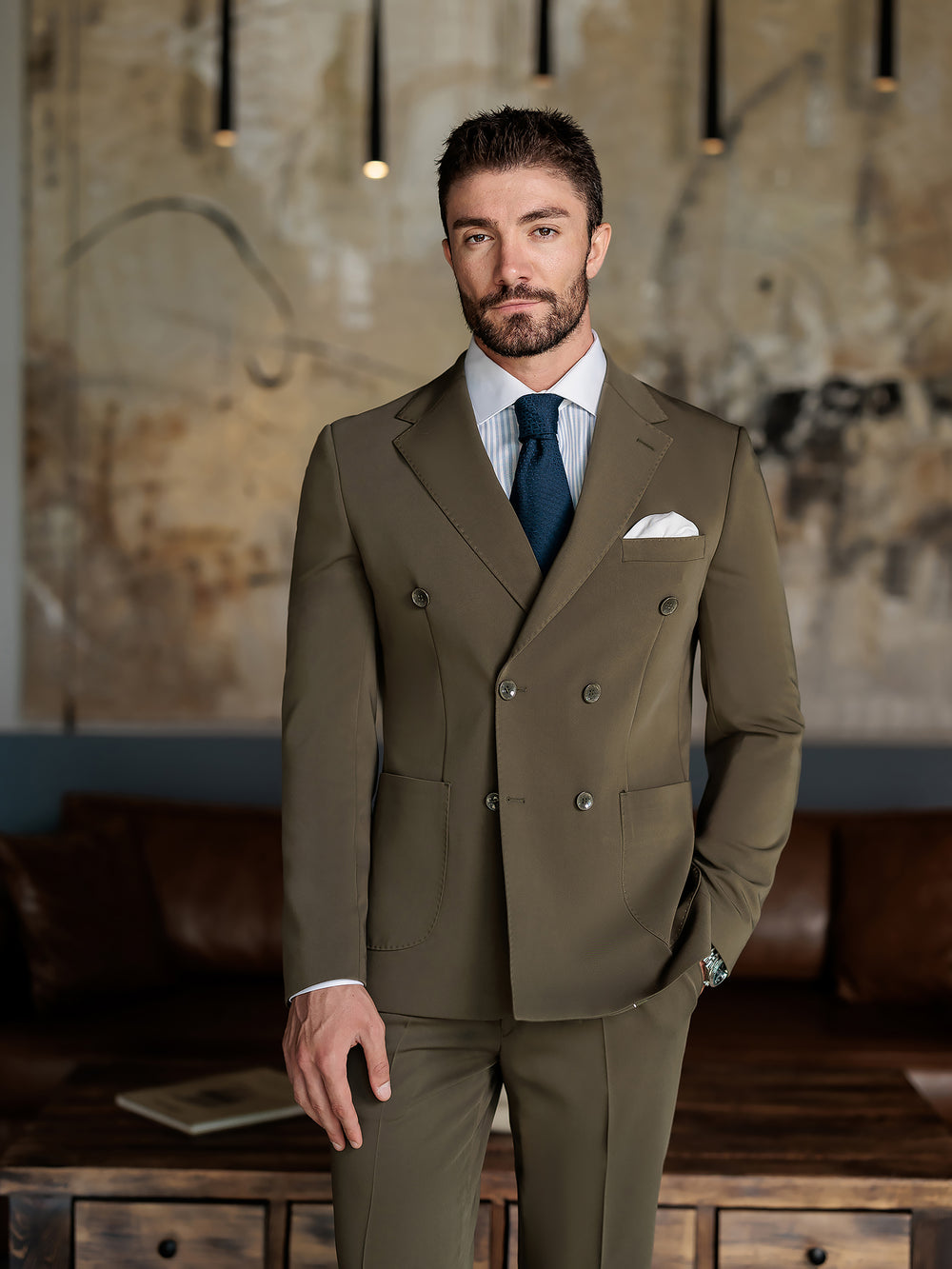 XAYWEAR double-breasted olive suit for men with white shirt and navy tie in modern indoor setting