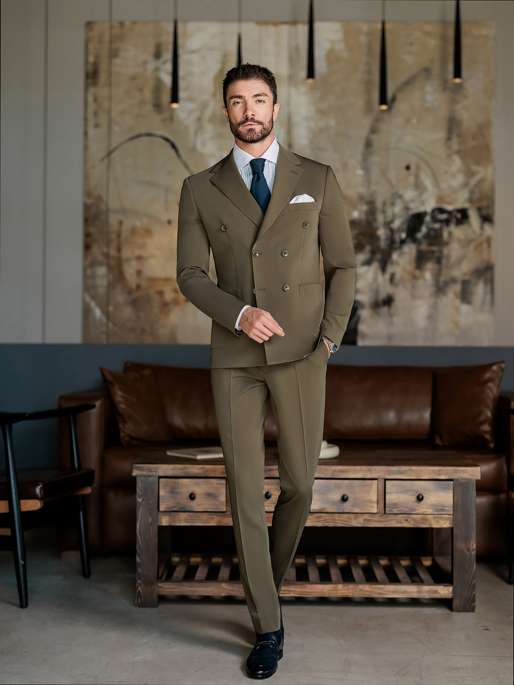 Man wearing an olive double-breasted suit for men by XAYWEAR standing in a modern living room