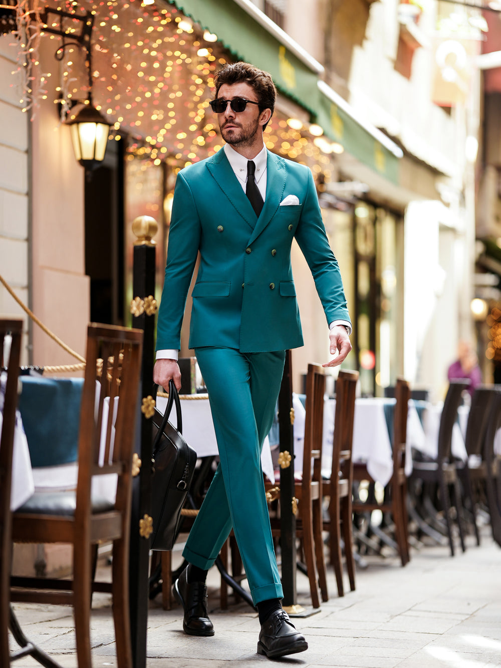 Man wearing a stylish teal suit for men by XAYWEAR walking confidently in outdoor cafe setting