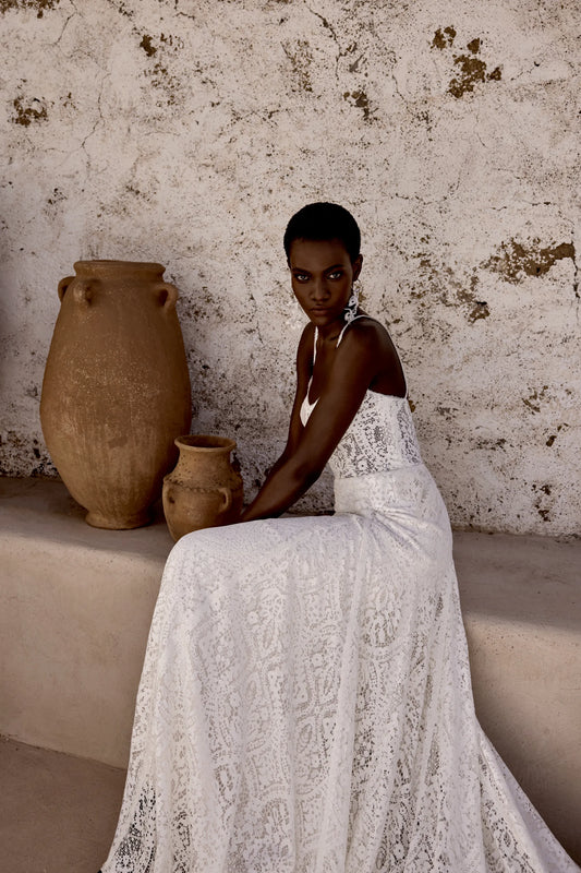XAYWEAR elegant white lace wedding gown worn by model sitting next to rustic clay pots