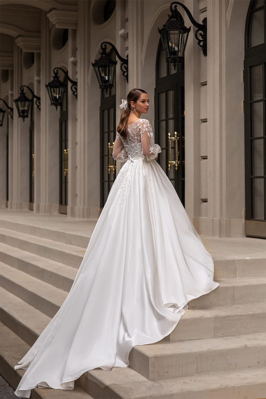 Elegant XAYWEAR wedding gown with long train and lace details worn by bride on stone steps