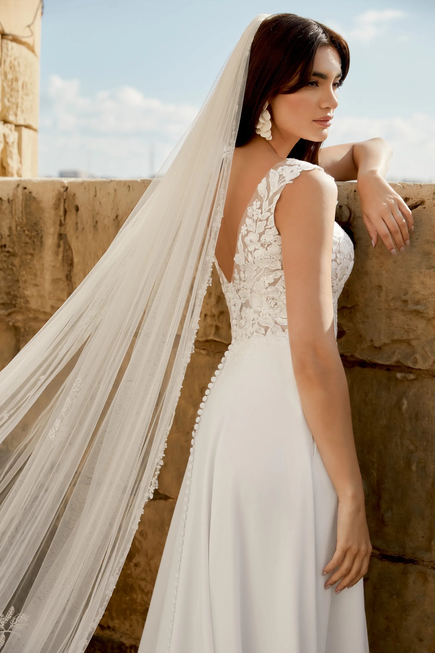 Elegant bridal gown with lace details and long veil worn by woman standing outdoors