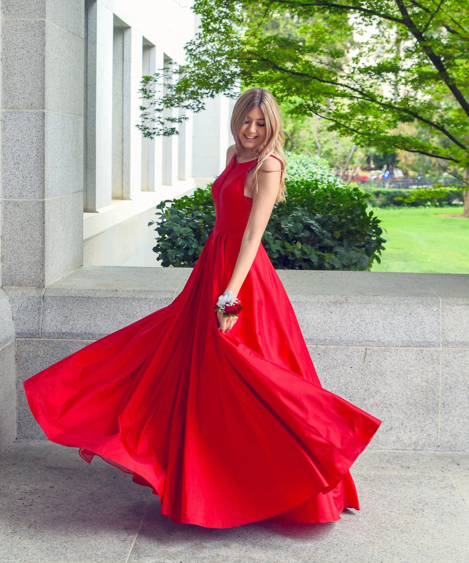 Women premium elegant red gown worn by a woman twirling outdoors near stone building and greenery