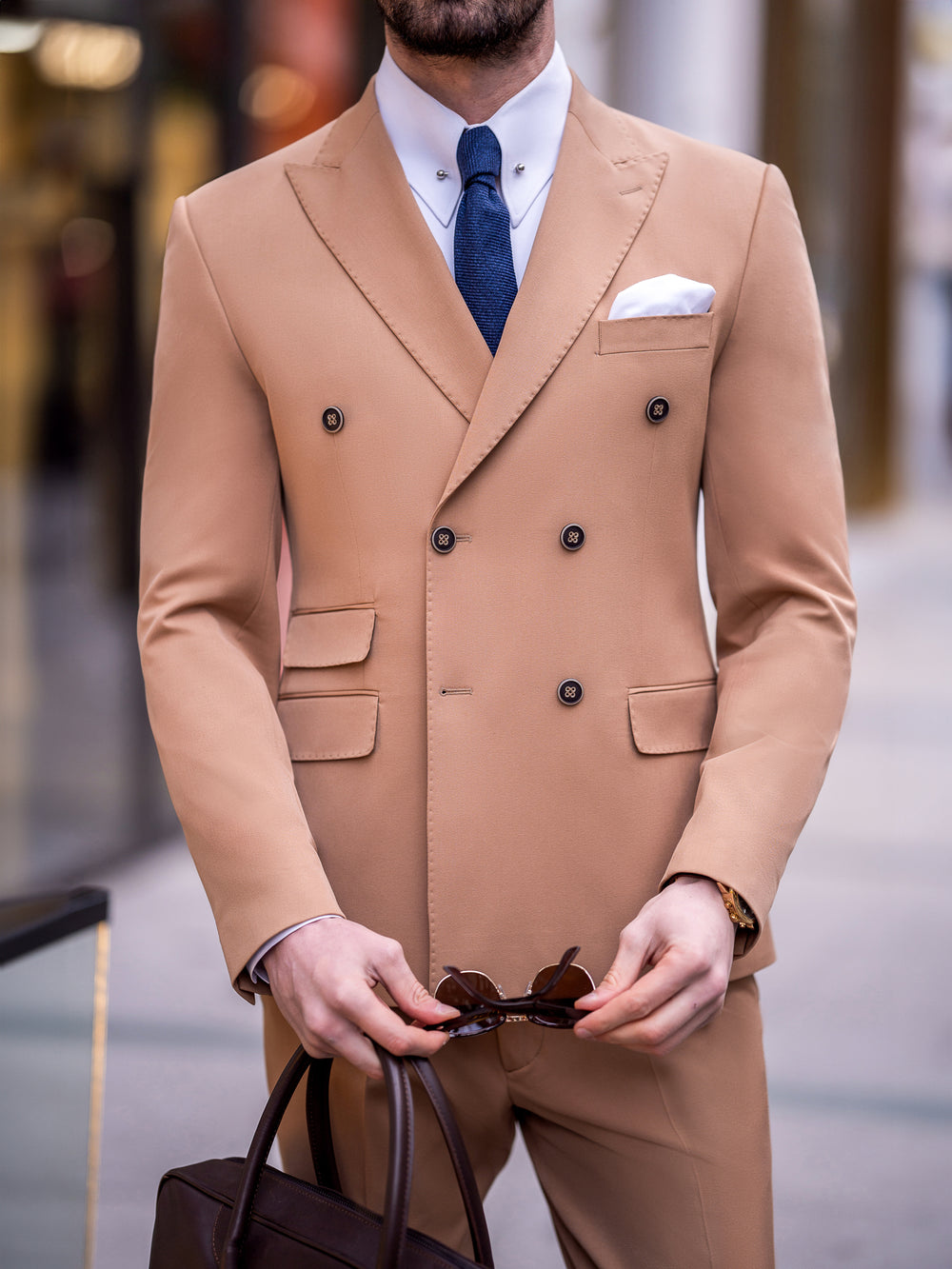 XAYWEAR tan double-breasted suit for men with white shirt and navy tie holding brown bag