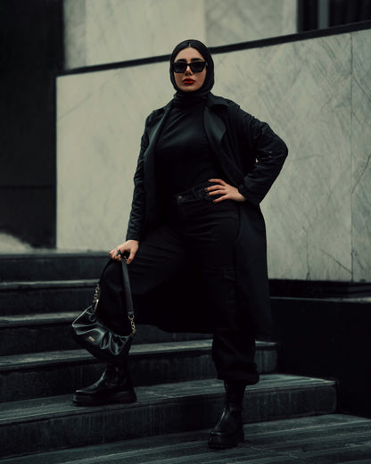 Stylish black coat for women by XAYWEAR worn with black pants and boots on city stairs