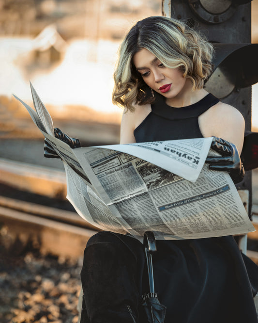 Woman wearing a black dress by XAYWEAR reading a newspaper while sitting outdoors
