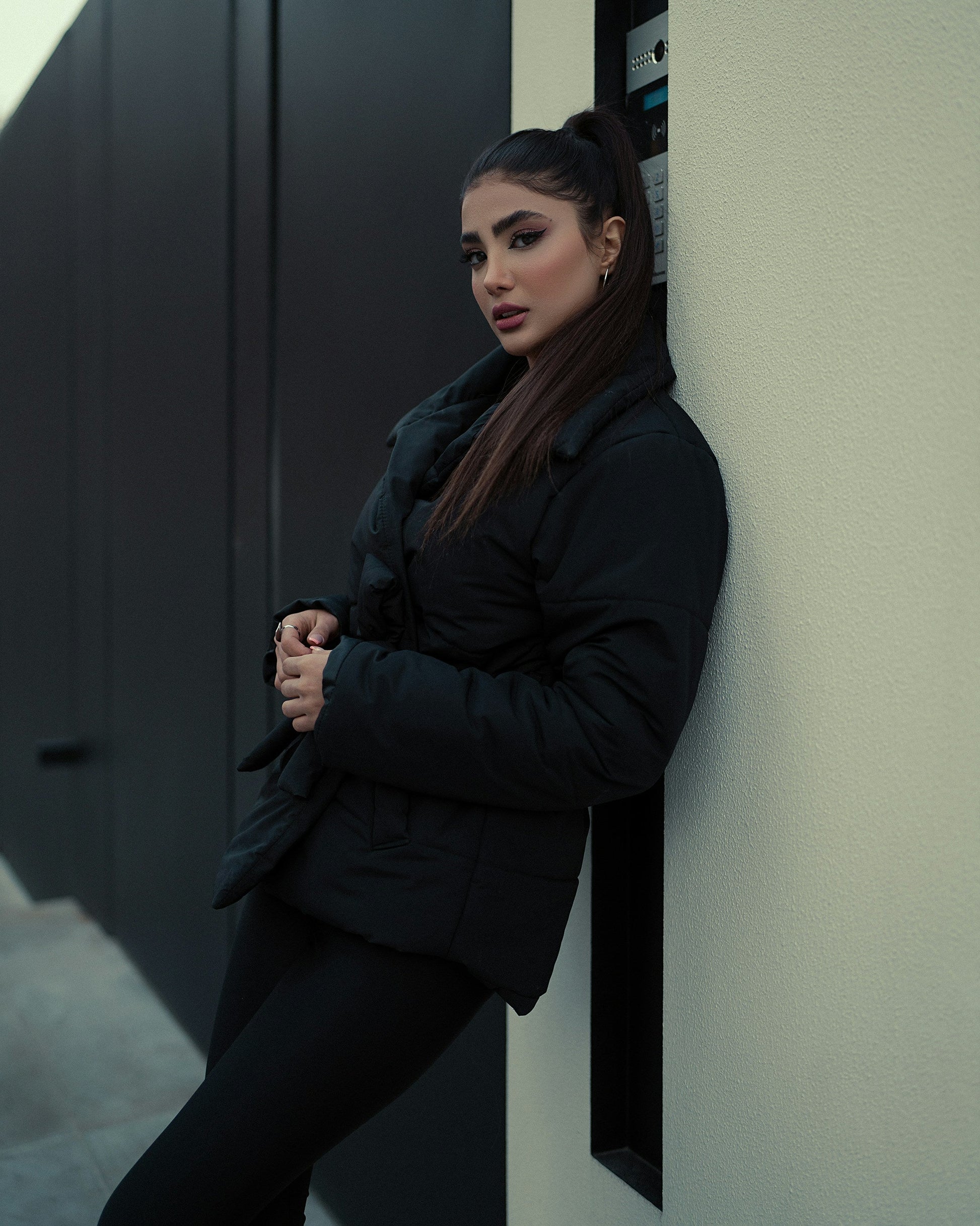 XAYWEAR black puffer jacket for women worn by model leaning against wall in urban setting