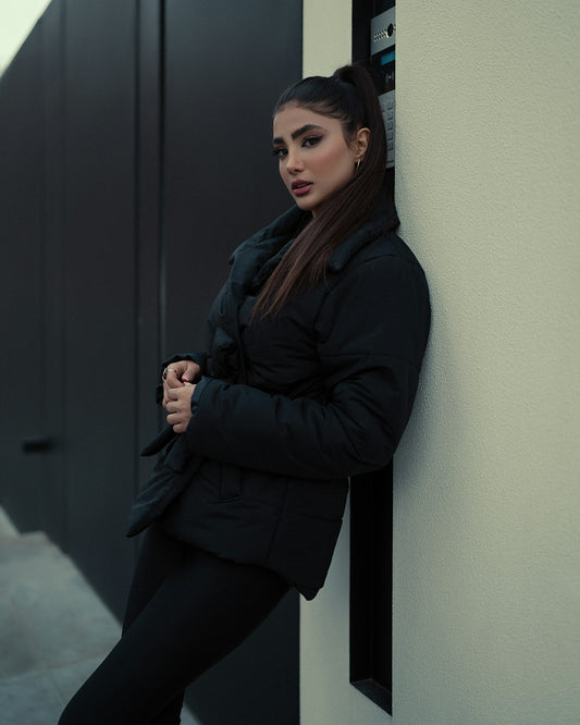 XAYWEAR black puffer jacket for women worn by model leaning against wall in urban setting