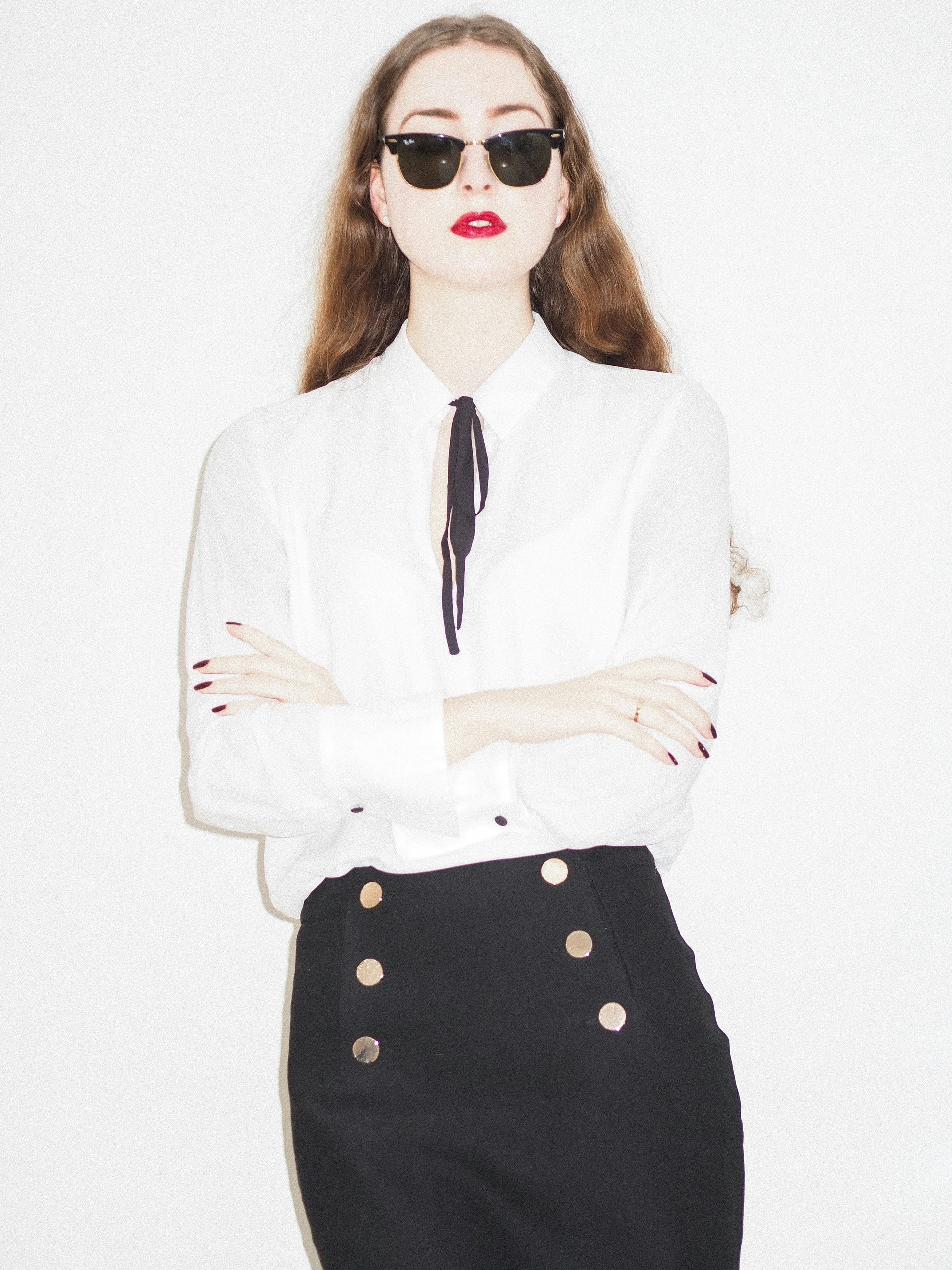 XAYWEAR black skirt mini-skirt featuring gold button details worn with a white blouse and sunglasses