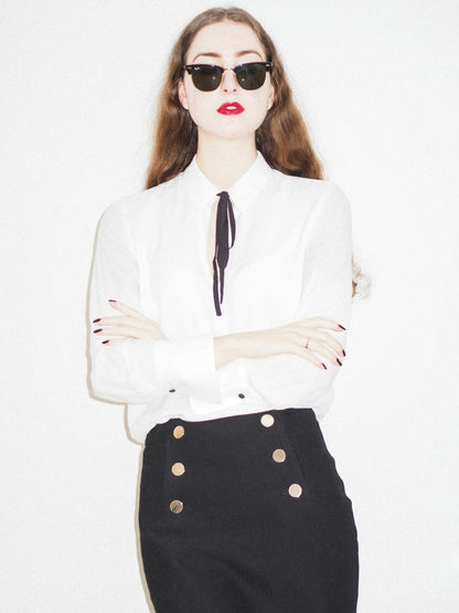XAYWEAR black skirt mini-skirt featuring gold button details worn with a white blouse and sunglasses