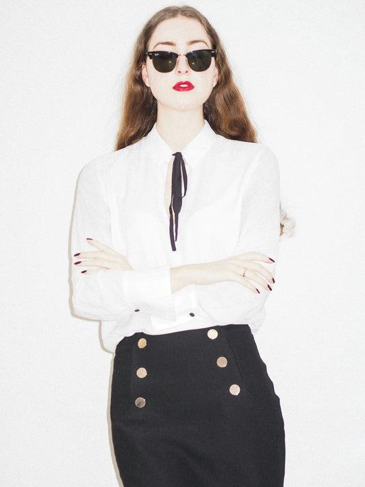 XAYWEAR black skirt mini-skirt featuring gold button details worn with a white blouse and sunglasses