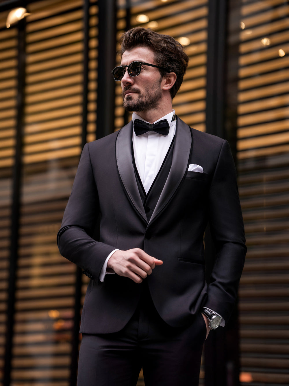Stylish man wearing a black three piece suit for men by XAYWEAR with bow tie and sunglasses