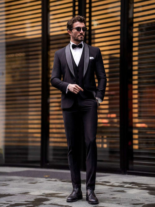 Man wearing a black three piece suit for men by XAYWEAR with bow tie and sunglasses standing outdoors