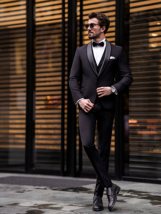 Man wearing black three piece suit for men with bow tie and sunglasses standing outdoors