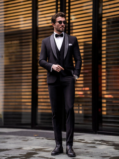 Man wearing a black three piece suit for men with bow tie and sunglasses standing outdoors