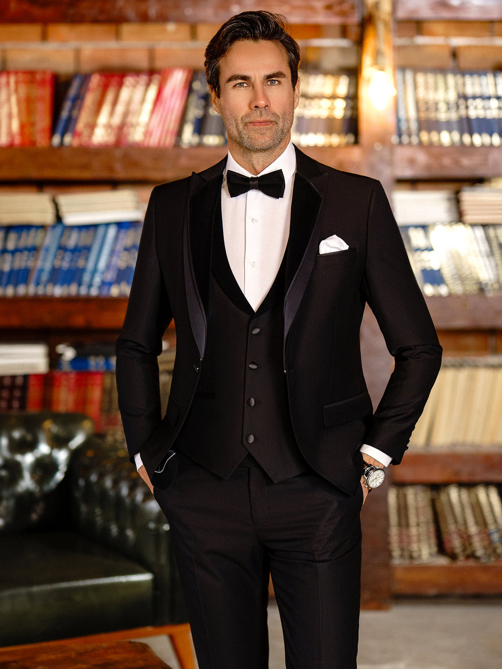 XAYWEAR black tuxedo suit for men with bow tie, white shirt, and pocket square in library setting