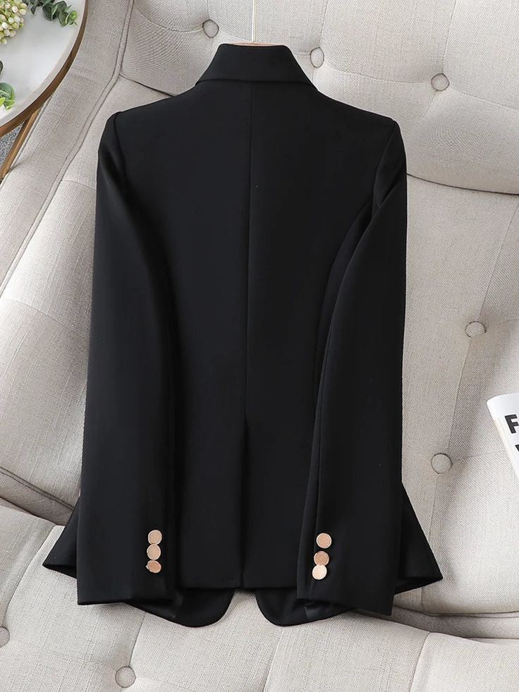Black women blazer by XAYWEAR with gold buttons on sleeves laid flat on beige couch