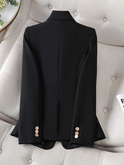 Black women blazer by XAYWEAR with gold buttons on sleeves laid flat on beige couch