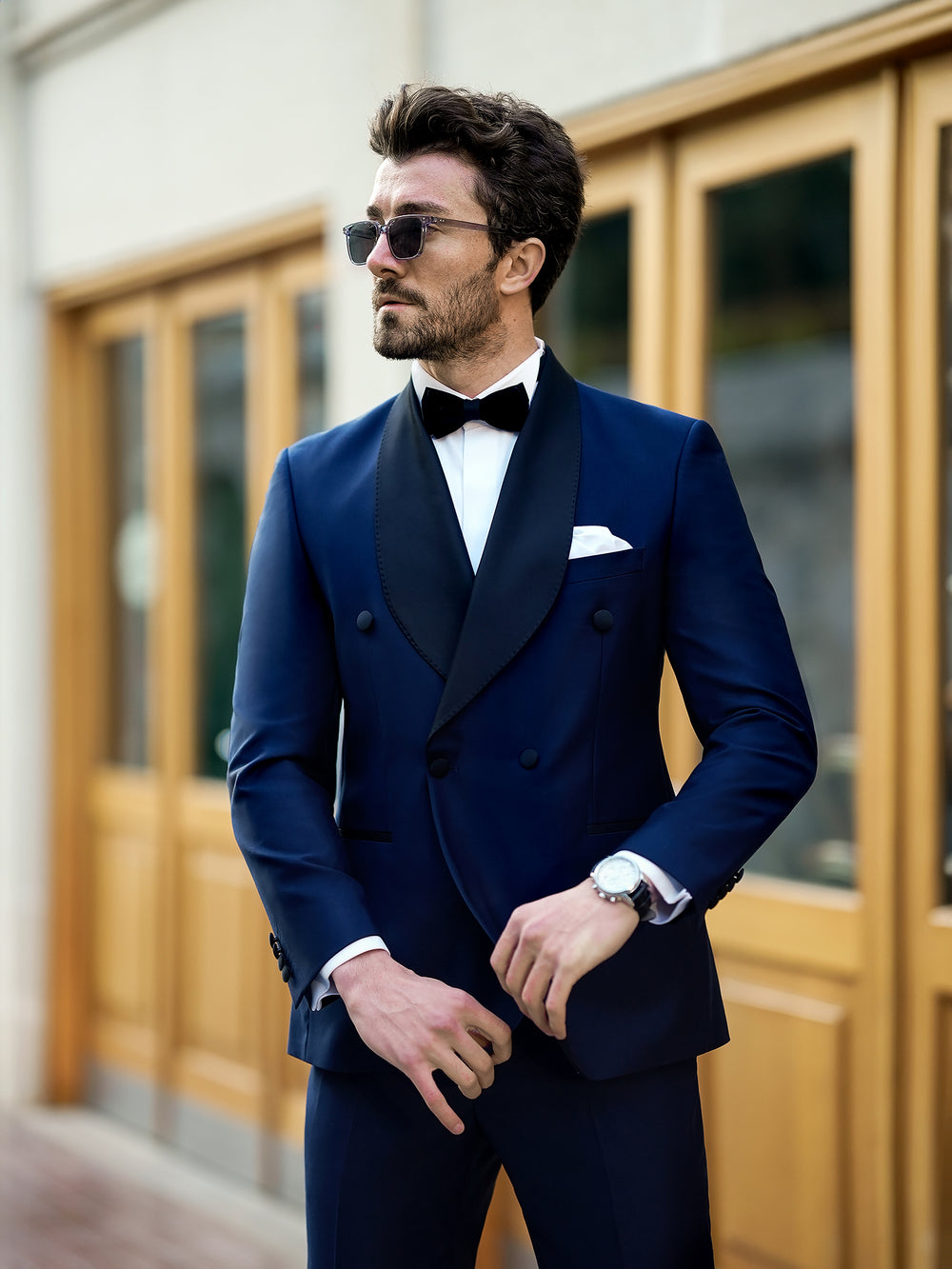 Stylish man wearing a tailored blue suit for men by XAYWEAR with black lapels and bow tie