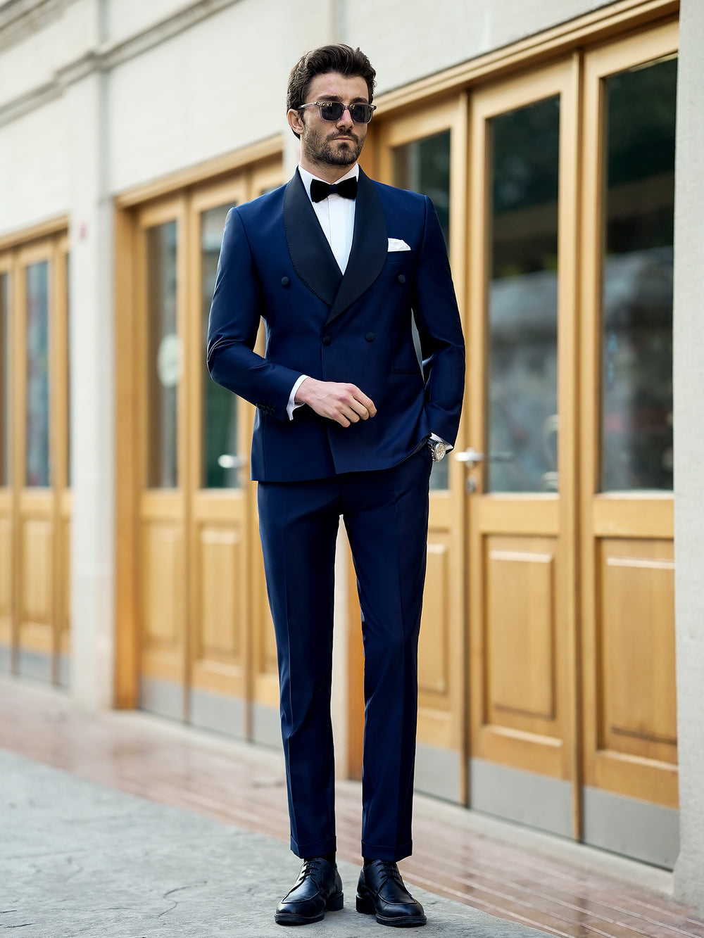 Man wearing stylish XAYWEAR blue suit for men with black lapels and bow tie standing outdoors