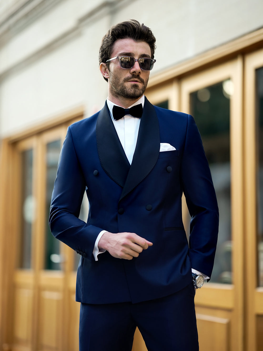 Man wearing XAYWEAR blue suit for men with black lapel and bow tie in urban setting