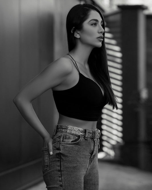 Woman wearing a black XAYWEAR crop top paired with high-waisted jeans and belt in side profile