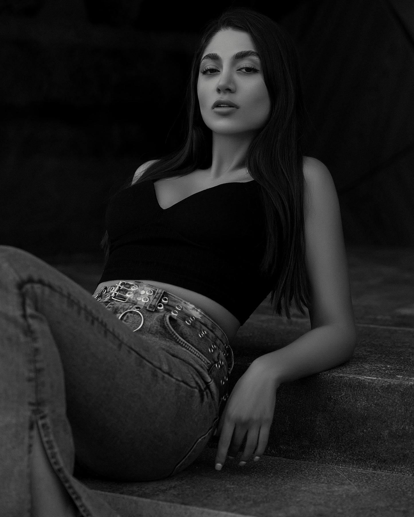 XAYWEAR black crop top worn by woman reclining on steps with high-waisted jeans and chain belt