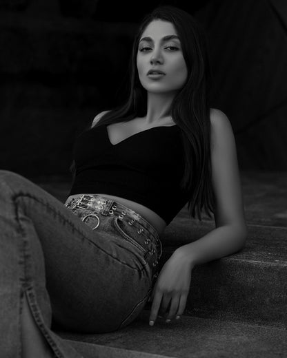 XAYWEAR black crop top worn by woman reclining on steps with high-waisted jeans and chain belt