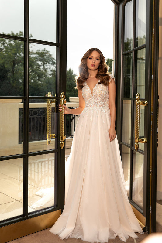 XAYWEAR bridal gown wedding dress with lace bodice and flowing skirt standing by glass doors