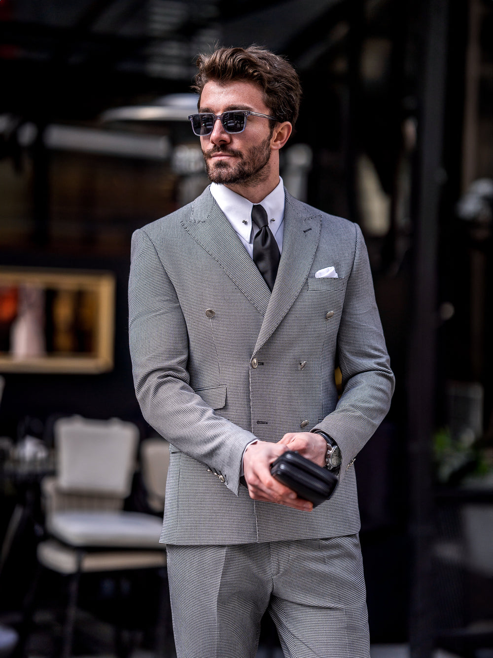 Man wearing a stylish gray double-breasted suit for men with black tie and sunglasses outdoors