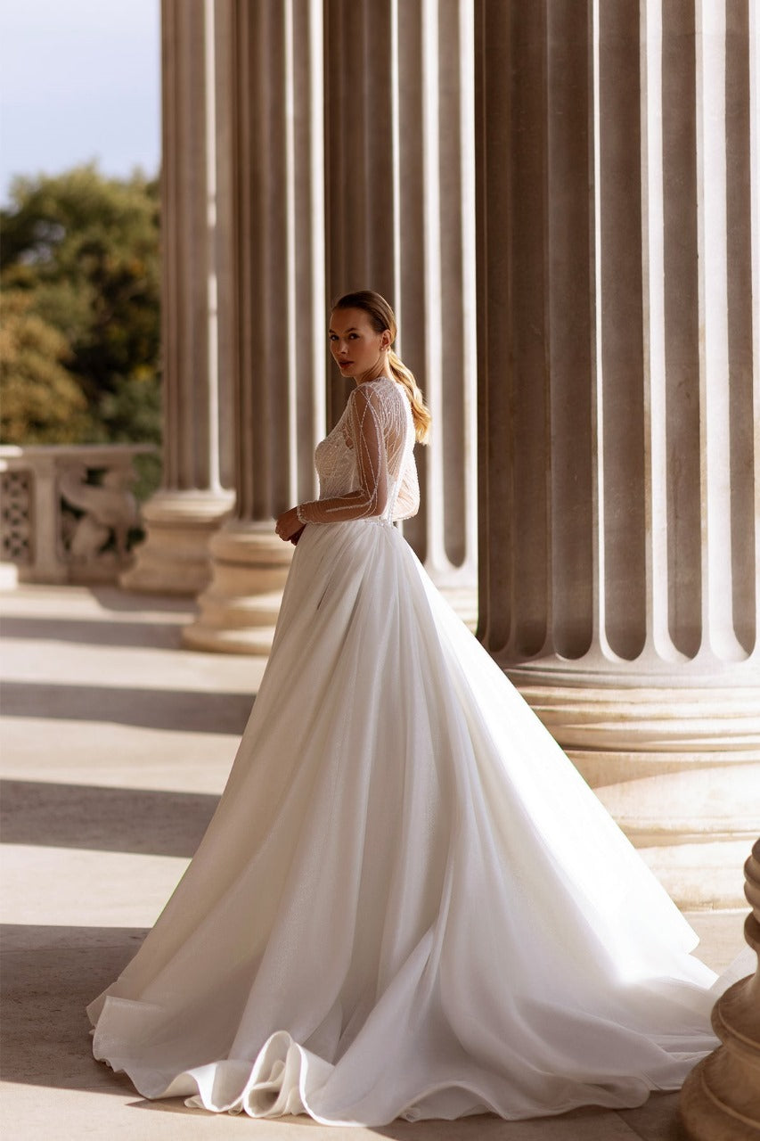 XAYWEAR elegant bridal gown with long lace sleeves and flowing skirt in grand architectural setting
