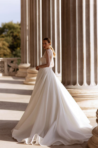 XAYWEAR elegant bridal gown with long lace sleeves and flowing skirt in grand architectural setting