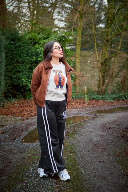 Woman wearing XAYWEAR brown winter jacket with teddy bear sweater and black track pants outdoors