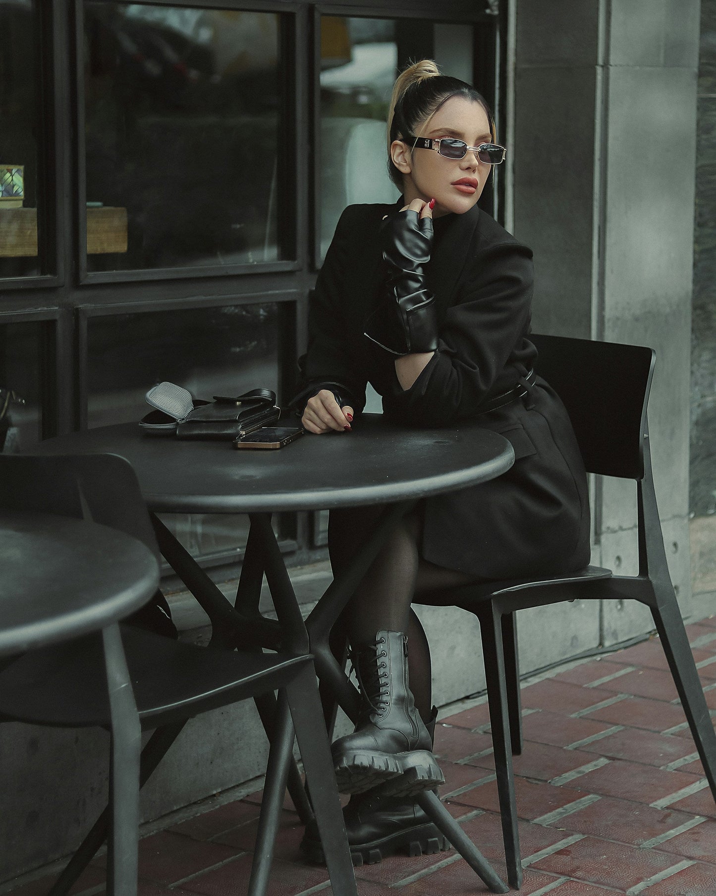Stylish woman wearing a fashionable black blazer women seated at a café with sunglasses and gloves