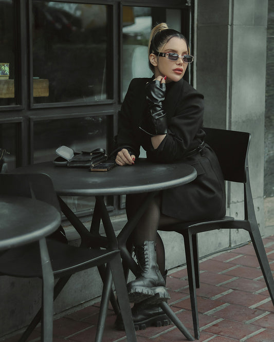 Stylish woman wearing a fashionable black blazer women seated at a café with sunglasses and gloves