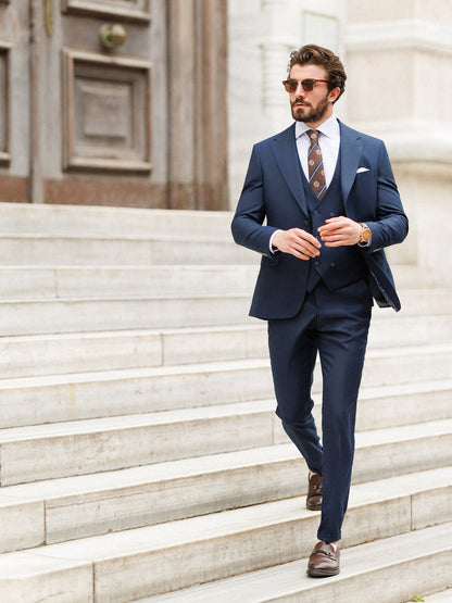 Man wearing XAYWEAR navy blue formal wedding suit with waistcoat and patterned tie walking down stone steps
