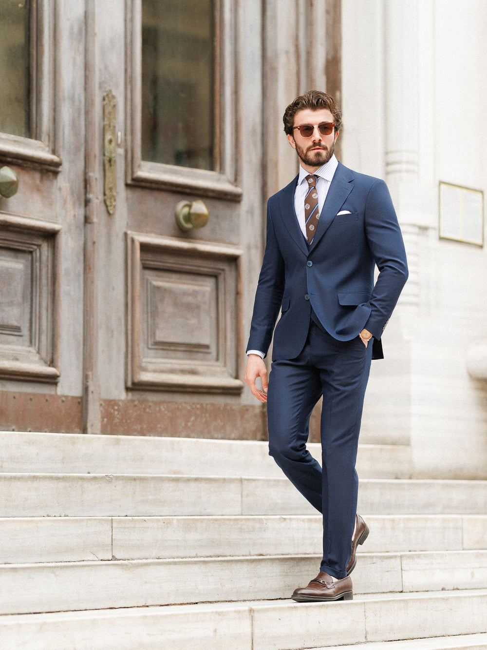 XAYWEAR navy formal wedding suit worn by man with brown shoes and sunglasses on stone steps