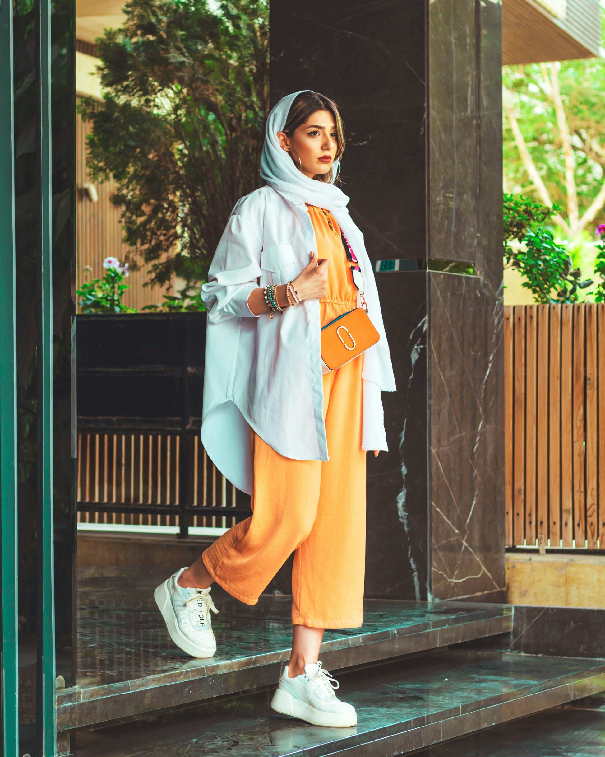Stylish woman wearing a lightweight overshirt jacket paired with orange pants and white sneakers