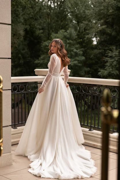 XAYWEAR bridal gown with long sheer sleeves and flowing train worn outdoors on balcony