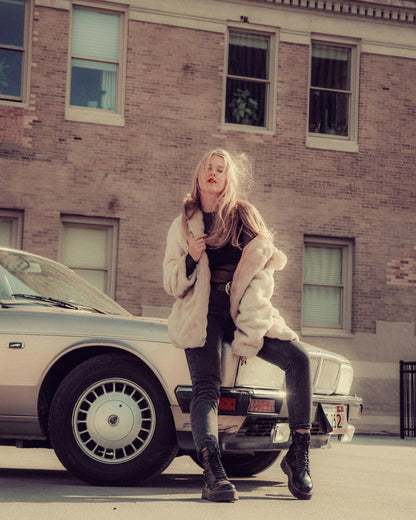 Woman wearing beige XAYWEAR women coat standing next to vintage car in urban setting