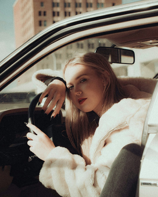 Woman wearing a white fluffy women coat sitting inside a car by XAYWEAR