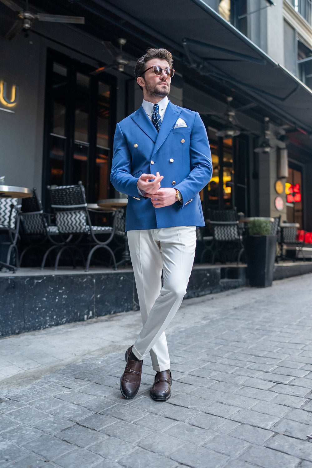 Man wearing a stylish blue double-breasted men blazer suit with white pants and brown shoes outdoors