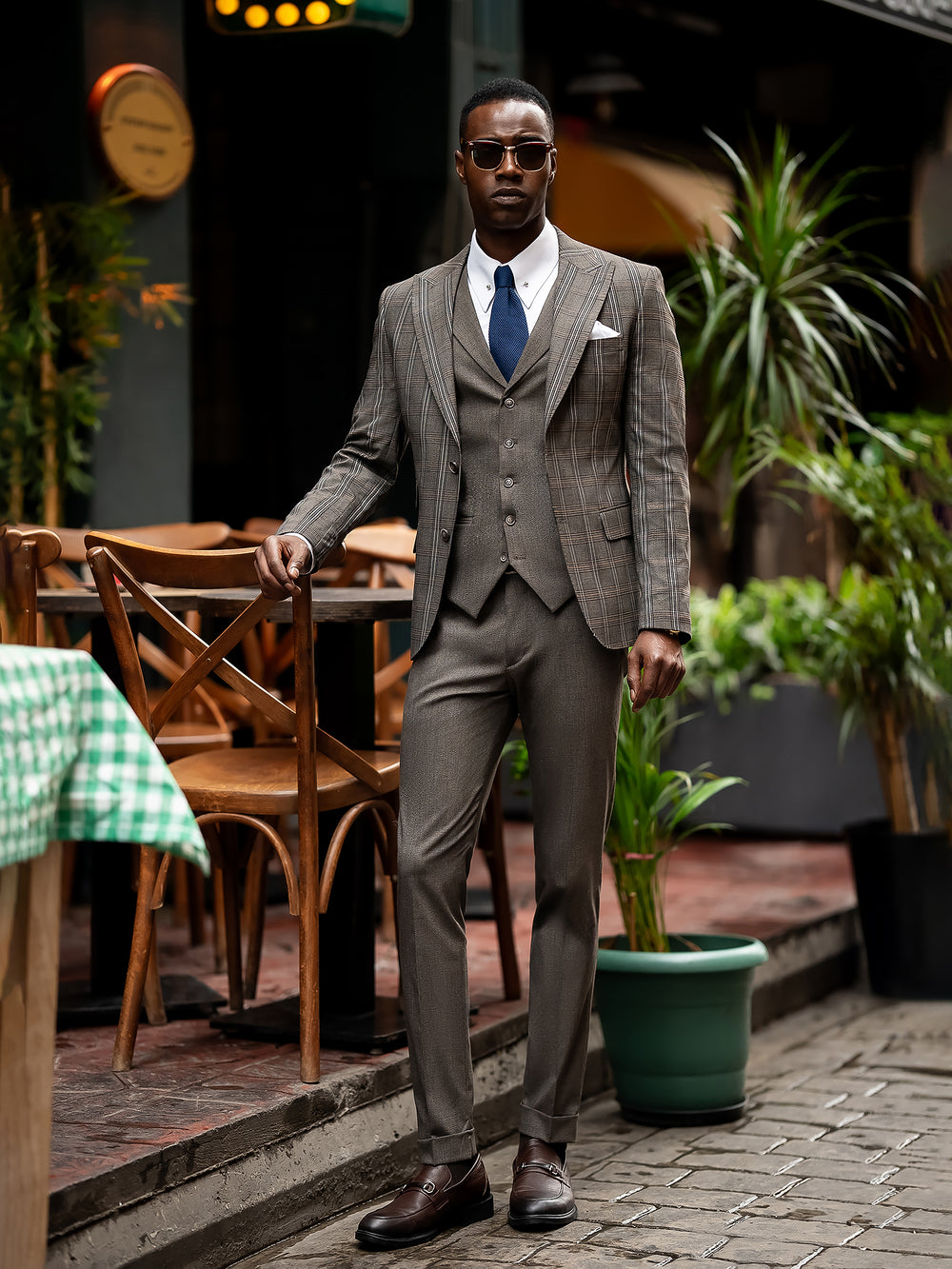 XAYWEAR men suit in brown plaid with white shirt and blue tie worn by man in sunglasses outdoors